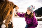 Ein Mädchen streichelt im Schnee ein Pony – ein magischer Moment im Familienhotel Alpura Retreat in Südtirol.