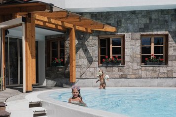 Zwei Kinder plantschen fröhlich im Außenpool des Familienhotels Tirolerhof vor beeindruckender Bergkulisse