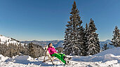 Eine Frau sitzt im Stuhl geniest die Sonne. Der Wald ist Schnee bedeckt.