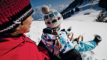 Ein Kind beim Rodeln mit einem Erwachsenen im Winter. Die beiden befinden sich am Ofterschwanger Horn im Allgäu.