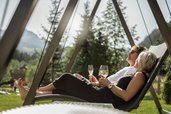 Entspannt genießen Eltern ein Glas Wein auf der Schaukelliege – ein Sommermoment im Familienhotel Alpura Retreat in Südtirol.