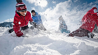 Kinder spielen im Schnee im Winter und haben Spaß. Allgäu bietet sich für jeden Winterurlaub mit der Familie an.
