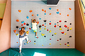 Zwei Kinder klettern die Kletterwand in der Indoor-Spielhalle vom Familienhotel Das Bayrischzell in Oberbayern hoch.