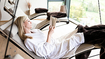 Frau liegt auf einer Liege im Wellnessbereich des Familienhotels und liest ein Buch.
