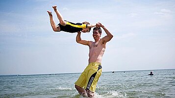 Ein Vater spielt mit seinem Sohn im Wasser an der Ostsee bei einem Kurzurlaub mit Kind. 