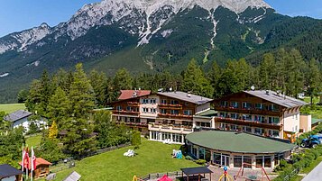 Luftaufnahmen des Familienhotels Lärchenhof in Tirol. Das Hotel ist umgeben von einer großzügigen Grünfläche und einem schönen Bergpanorama.