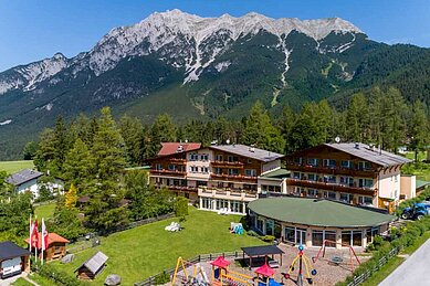 Luftaufnahmen des Familienhotels Lärchenhof in Tirol. Das Hotel ist umgeben von einer großzügigen Grünfläche und einem schönen Bergpanorama.