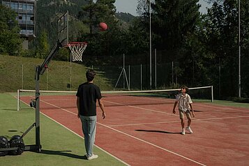 Vater spielt gemeinsam mit seinem Sohn auf dem Sportplatz des Familienhotels Engel Gourmet & Spa Basketball.