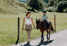 Eine Erwachsene begleitet ein Kind auf einem Pony auf einem Weg im Außenbereich des Familienhotels Oberkarteis im Salzburger Land.