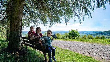 Wandern in der Rhön: Kinder ruhen sich auf einer Bank aus. Mit einem herrlichen Blick eine kleine Pause genießen.