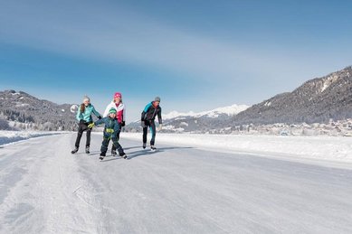 Eine Familie genießt den Winter beim Eislaufen auf einem zugefrorenen See mit traumhafter Bergkulisse in Kärnten