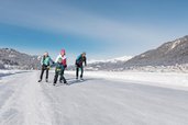 Eine Familie genießt den Winter beim Eislaufen auf einem zugefrorenen See mit traumhafter Bergkulisse in Kärnten