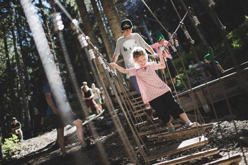 Ein Mädchen balanciert im Outdoor-Kletterpark zwischen Seilen und Holzelementen im Familienurlaub im Wellness- & Familienhotel Egger.