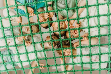 Kinder haben Spaß im Indoor-Spielbereich und schauen lachend durch ein großes Kletternetz im Familienhotel Friedrichshof.