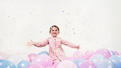 Ein Mädchen freut sich über viele Luftballons und Konfetti.