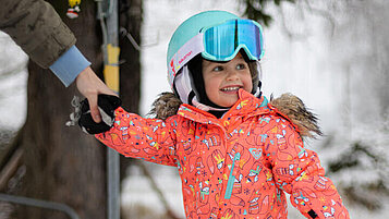 Kleines Mädchen auf Skiern beim Skikurs im Familienurlaub in der Steiermark wird an der Hand gehalten.