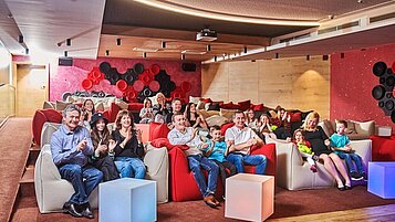 Eltern und Kinder sitzen im Kino / Theatersaal und sehen sich eine Vorstellung an im Familienhotel Aigo welcome family in Oberösterreich