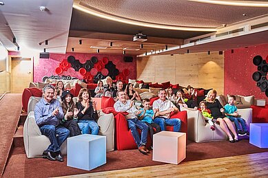 Eltern und Kinder sitzen im Kino / Theatersaal und sehen sich eine Vorstellung an im Familienhotel Aigo welcome family in Oberösterreich