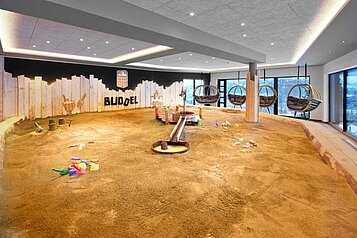 Großer Indoor-Sandkasten mit einem Wasserbrunnen, vielen Spielsachen und Hängekörben für Eltern im Familienhotel Allgäuer Berghof.