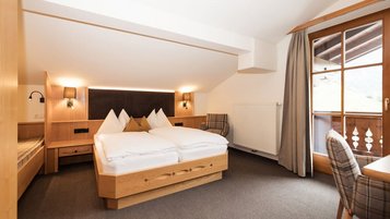 Gemütliches Familienzimmer im Familienhotel Oberkarteis mit Doppelbett, Balkon und hellen Holzmöbeln für eine erholsame Auszeit.