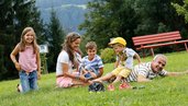 Familie spielt barfuß auf der Wiese vor dem Familienhotel Ramsi inmitten der Natur