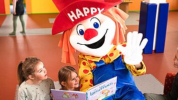 Clown Happy liest zwei Mädchen ein Buch vor