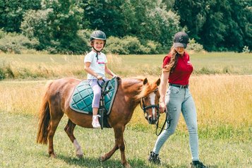 Ein Mädchen reitet fröhlich auf einem Pony über die Wiese des Familienhotel Friedrichshof.