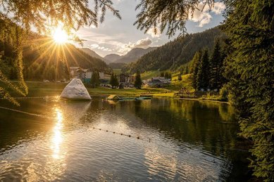 Ein Badeteich am Zauchenseehof im Salzburger Land liegt in der Abendsonne vor einer Bergkulisse.