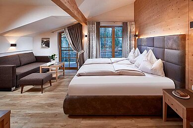 Einladendes, modernes Hotelzimmer im Hotel Habachklause im Salzburger Land mit einem großen Bett, einer gemütlichen Sitzecke und einem Holzbalkon mit Aussicht auf die Natur.
