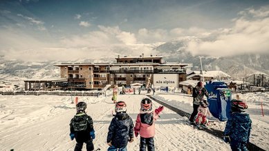 Kinder beim Skikurs direkt am Familienhotel Mia Alpina in Tirol vor verschneiter Bergkulisse.