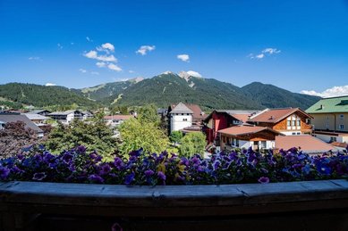Blick von einem Balkon auf Blumen, Häuser und Berge bei Das Kaltschmid in Tirol.