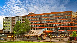 Außenansicht des Hotels Feldberger Hof im Schwarzwald, mit markanter moderner Architektur, umgeben von grünen Bäumen unter einem wolkigen blauen Himmel.