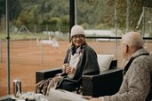 Eine Großmutter und ein Großvater sitzen entspannt auf der Terrasse des Hotel Sonngastein im Salzburger Land mit Blick auf die Tennisplätze.
