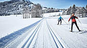 Menschen beim Langlaufen im Winter mit viel Schnee auf einer geräumten Strecke. Die Strecke ist am Unterjoch im Allgäu.