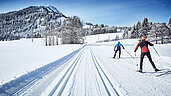 Menschen beim Langlaufen im Winter mit viel Schnee auf einer geräumten Strecke. Die Strecke ist am Unterjoch im Allgäu.