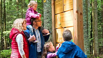 Familie beim Wandern im Naturpark Bayerischer Wald vor einer Infotafel.