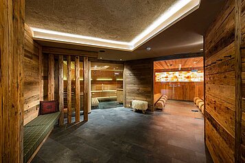 Luxuriöse Wellnessbereich-Eingang im Familienhotel Alphotel Tyrol in Südtirol mit rustikalen Holzwänden, stimmungsvoller Beleuchtung und entspannenden Ruhebereichen, die zum Verweilen einladen.