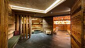 Luxuriöse Wellnessbereich-Eingang im Familienhotel Alphotel Tyrol in Südtirol mit rustikalen Holzwänden, stimmungsvoller Beleuchtung und entspannenden Ruhebereichen, die zum Verweilen einladen.