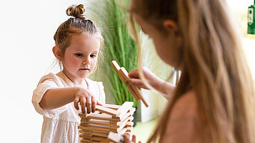 Mädchen baut in der Kinderbetreuung im Familienhotel mit Holzklötzen einen Turm.