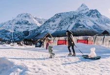 Eine Mutter zieht ihr Kind auf dem Schlitten durch den Schnee beim Familienhotel Tirolerhof, während ein weiteres Kind fröhlich vorausläuft