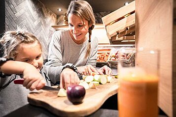 Mutter und Tochter schneiden frisches Obst am Frühstücksbuffet des Familienhotels Allgäuer Berghof.