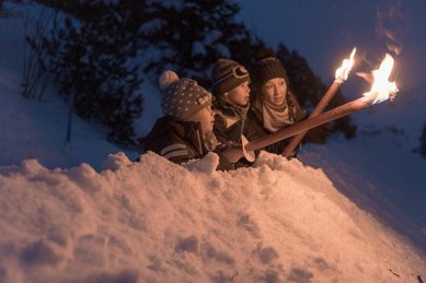 Familie mit Fackeln im Schnee beim Winterurlaub am Familienhotel Gorfion in Liechtenstein.