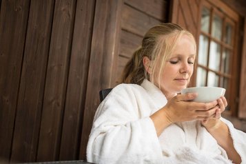 Frau im Bademantel genießt eine Tasse Tee auf der Terrasse des Familienhotel Ottonenhof.
