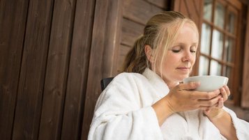 Frau im Bademantel genießt eine Tasse Tee auf der Terrasse des Familienhotel Ottonenhof.