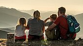 Familie in den Bergen macht eine Pause mit toller Aussicht in der Nähe des Familienhotels Almfamilyhotel Scherer in Tirol.