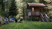 Ein Baumhaus auf einer grünen Wiese im Natur-Spielbereich des Kinderhotels Bruckwirt in Oberösterreich.
