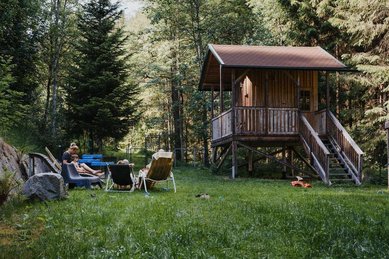 Ein Baumhaus auf einer grünen Wiese im Natur-Spielbereich des Kinderhotels Bruckwirt in Oberösterreich.