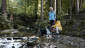 Wandern in Oberösterreich: Familie wandert durch den Hallerwald. Gemeinsam mit dem Hund kühlen sie sich am Bach ab.