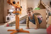 Kleiner Junge krabbelt durch ein Holzspielgerät im Spielzimmer des Familienhotels Elldus im Erzgebirge.