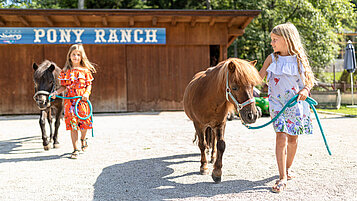 Zwei Mädchen gehen mit den Ponys im Hof spazieren im Familienhotel Galtenberg Family & Wellness Resort in Tirol.